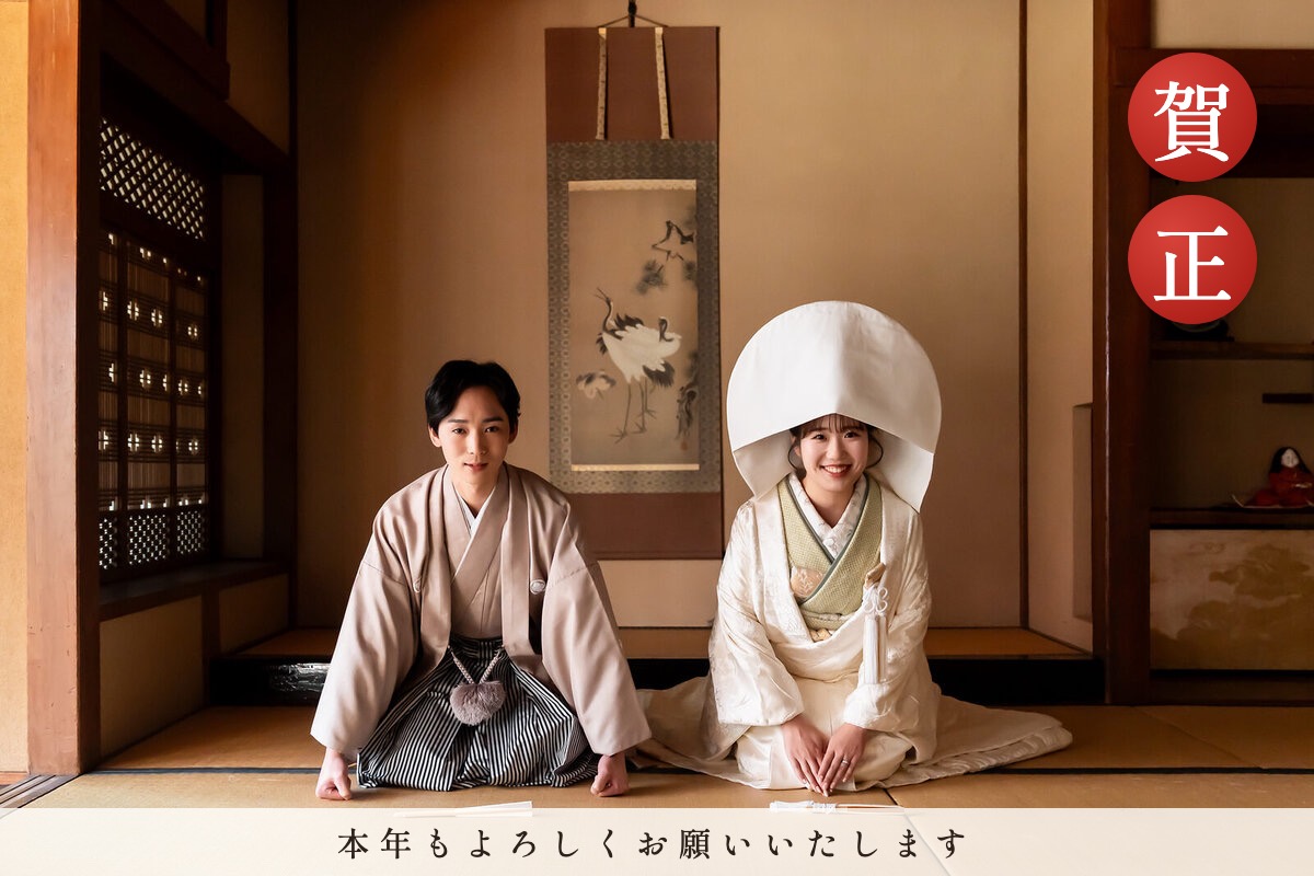 和室で正座してあいさつする白無垢と紋付袴のふたりに「賀正」と新年のあいさつを入れた年賀状の例